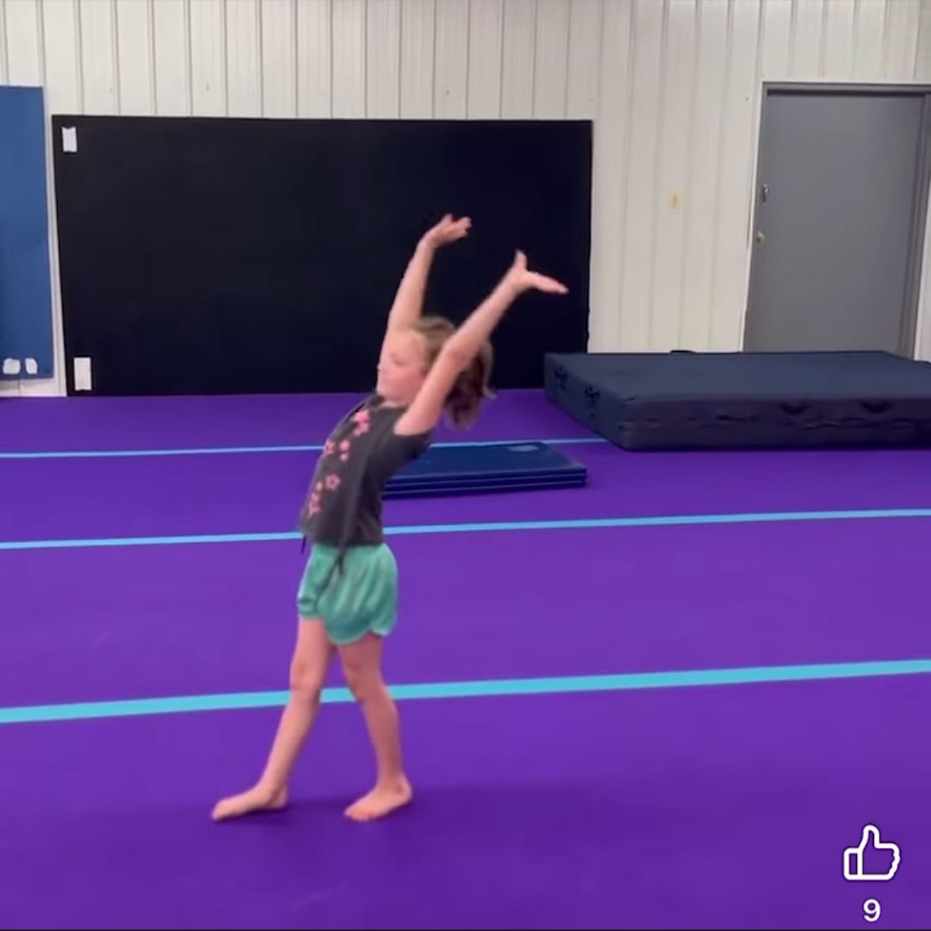 A young girl in a gym arches backward, hands overhead, preparing for a backbend on a purple mat.