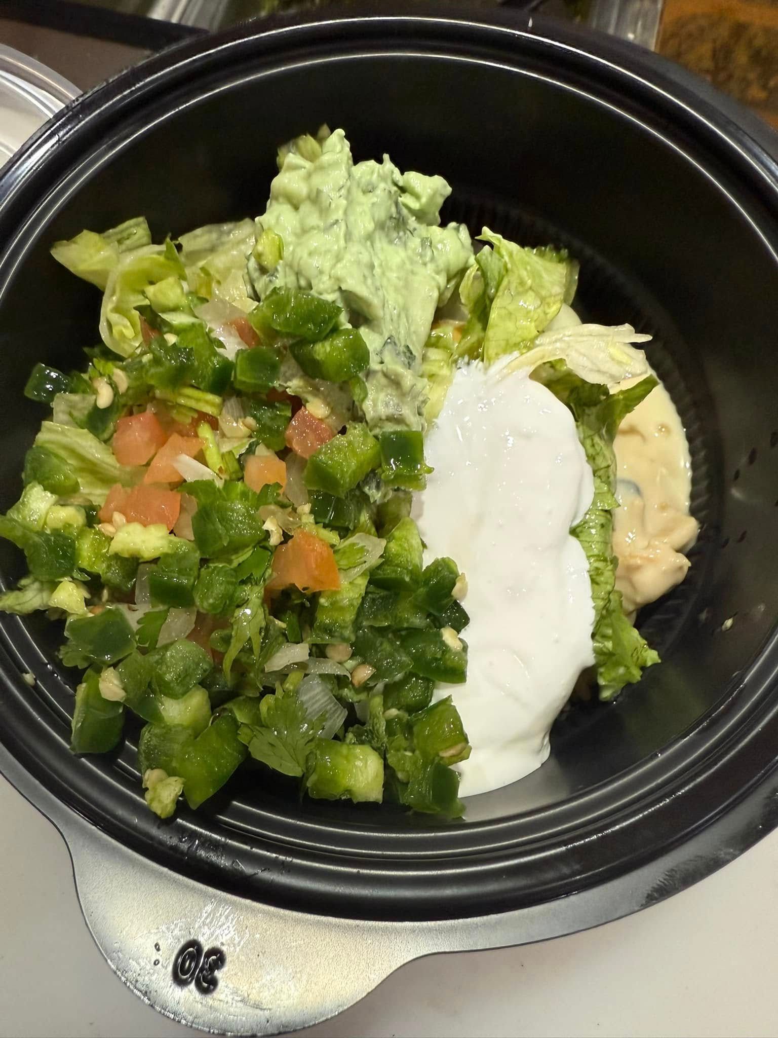 Salad in black bowl with green jalapeños, lettuce, avocado, and sour cream.