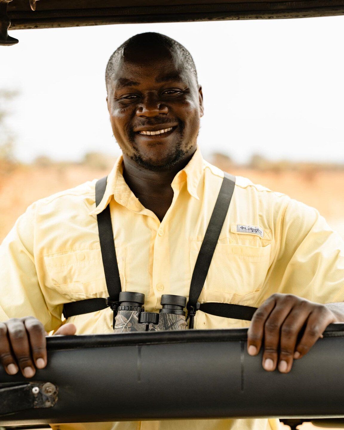 A man in a yellow shirt is holding binoculars and smiling.