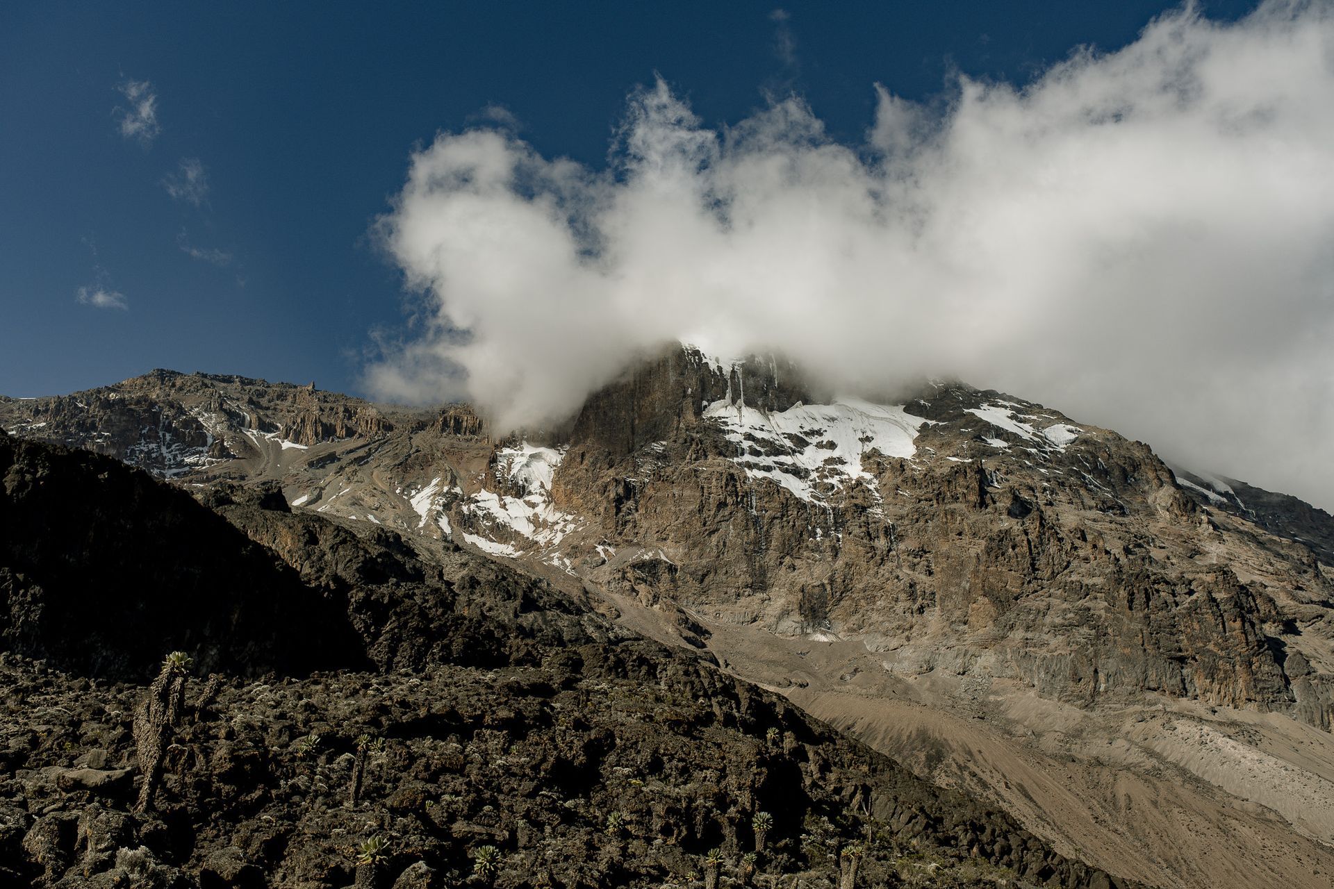 A mountain covered in snow and clouds with a blue sky in the background.