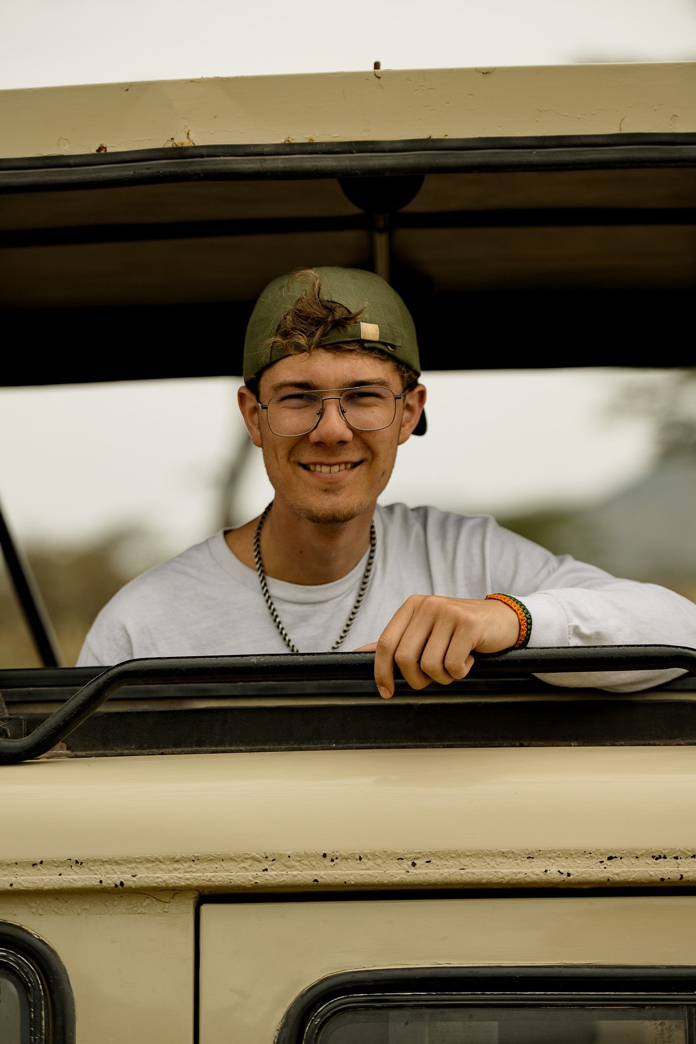 A young man wearing glasses and a hat is sitting in the back of a car.