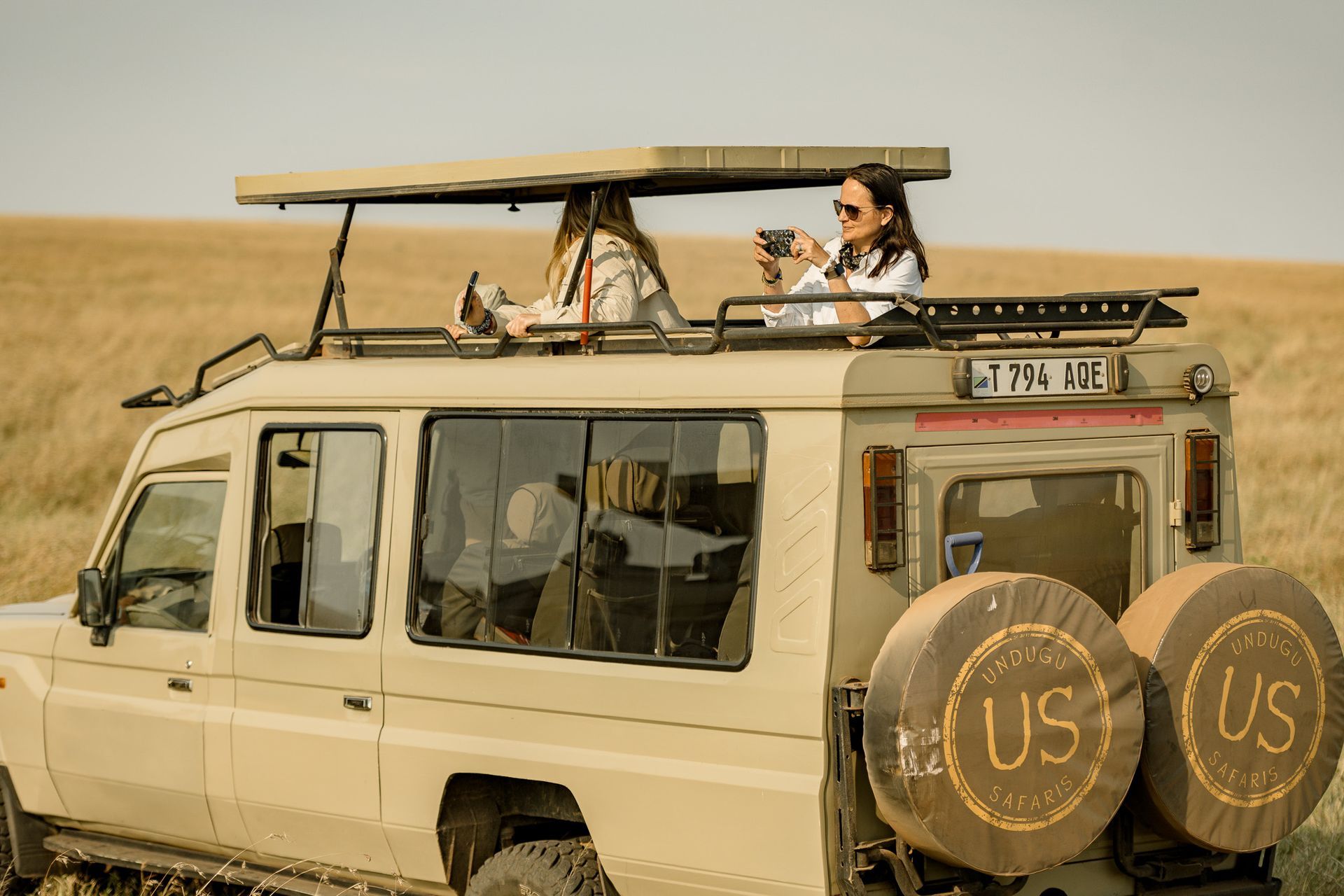 A woman is sitting on the roof of a jeep.