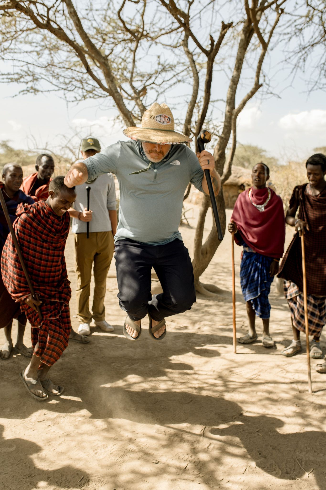 A man in a straw hat is jumping in the air in front of a group of people.