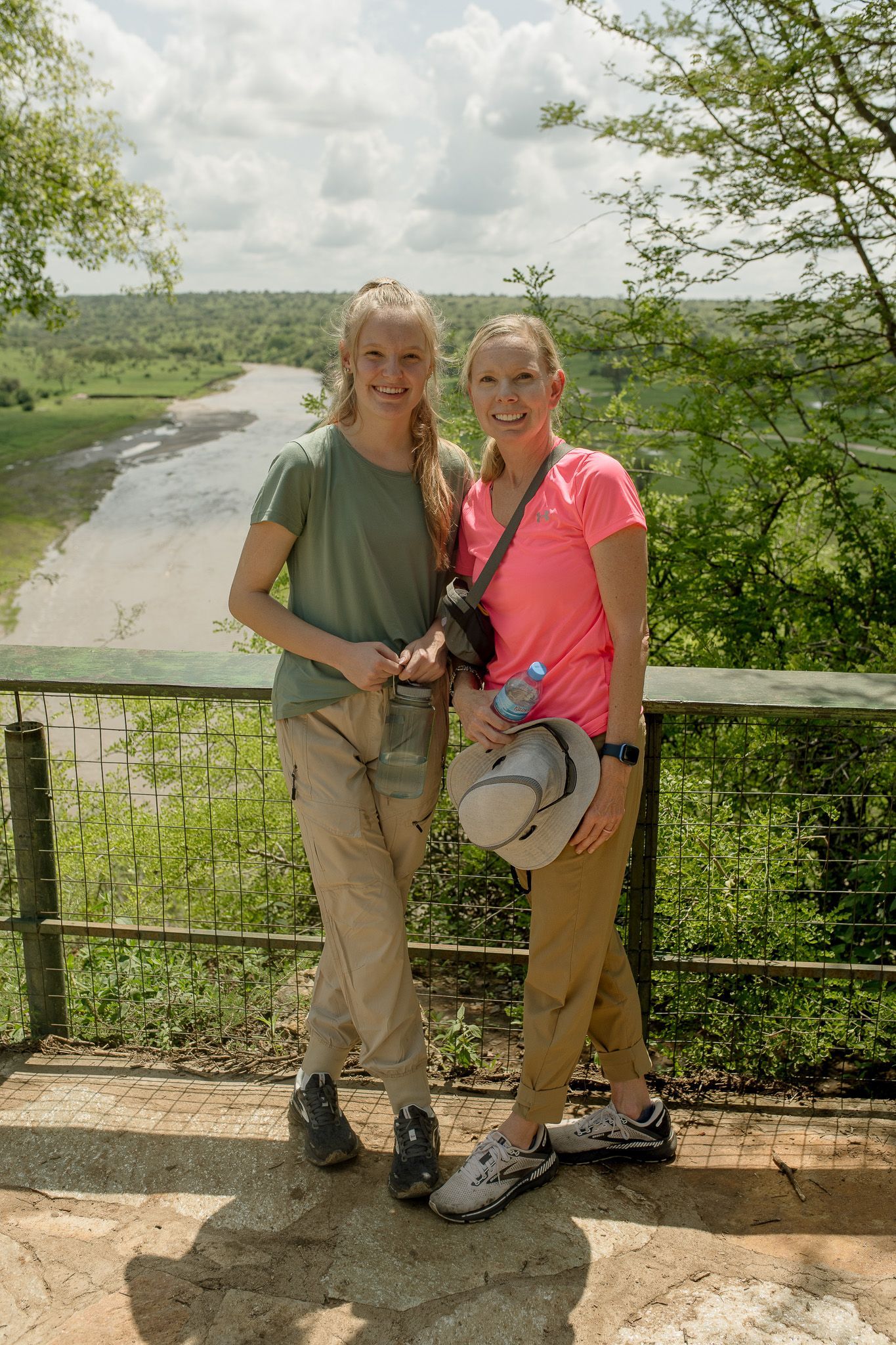 Two women are standing next to each other on a bridge overlooking a river.