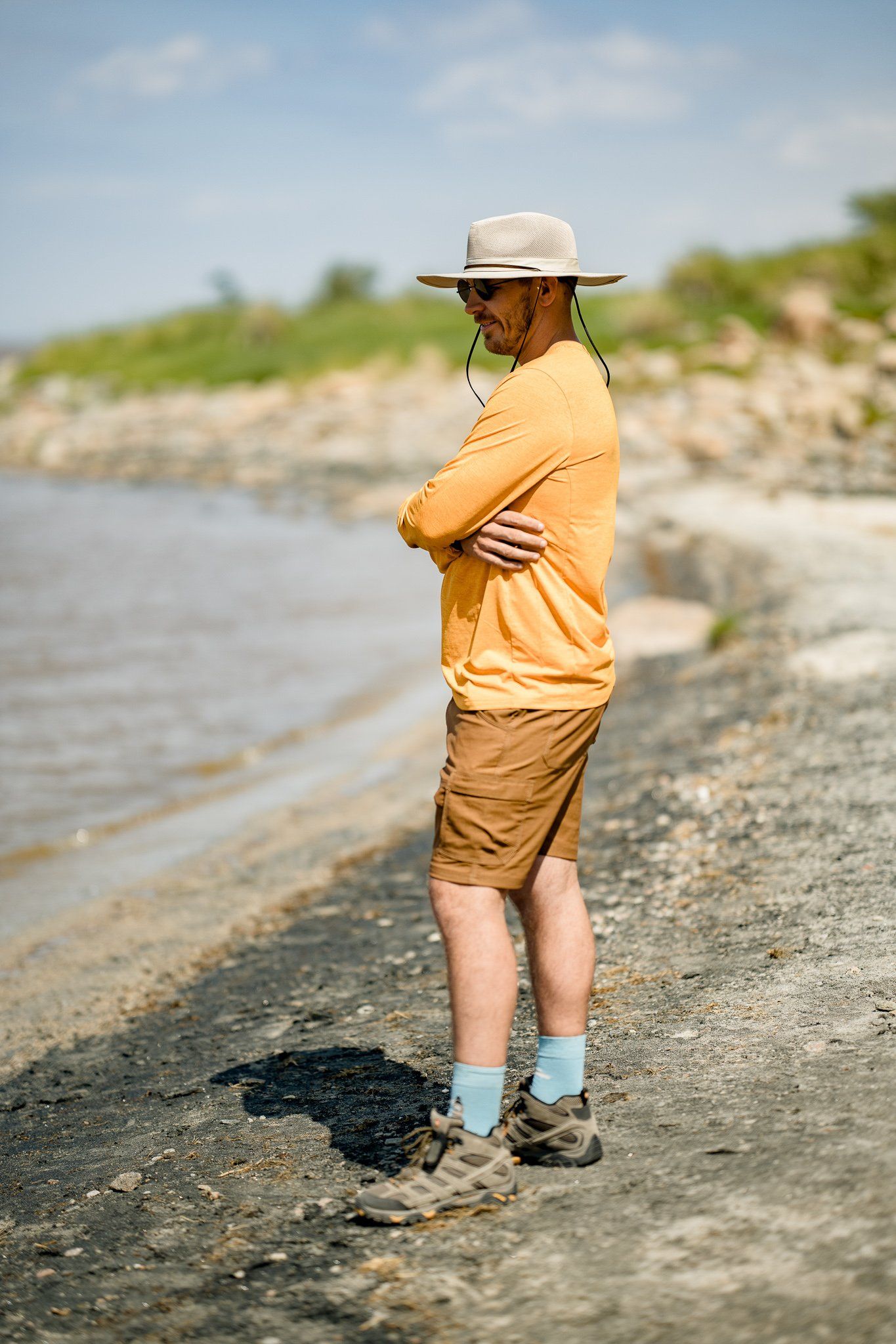 A man in a hat is standing on a beach with his arms crossed.