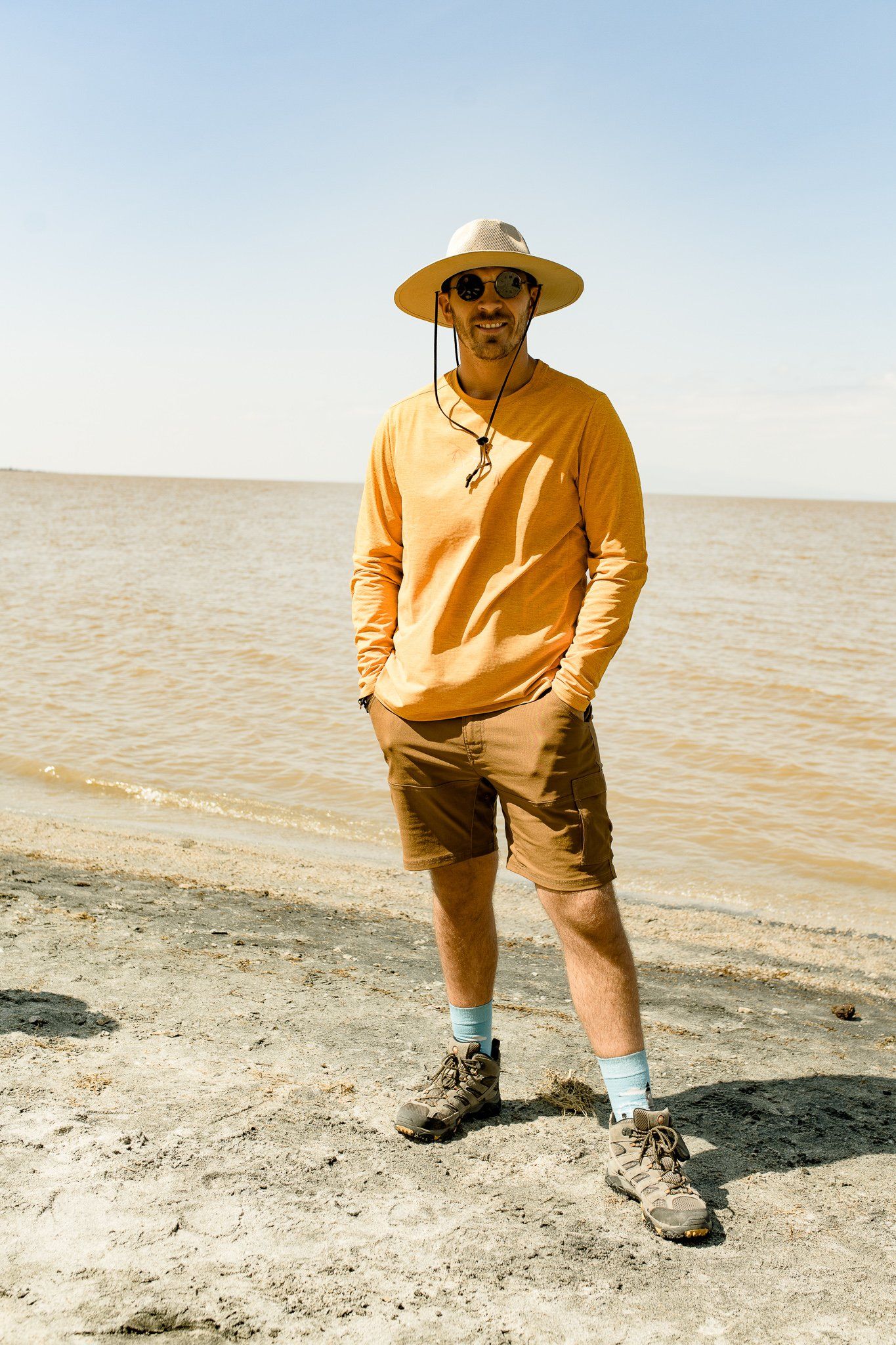 A man wearing a hat and sunglasses is standing on a beach.