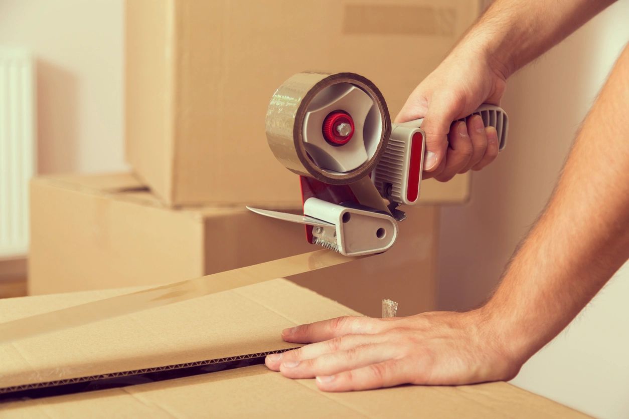 A person is using a tape dispenser to seal a cardboard box.