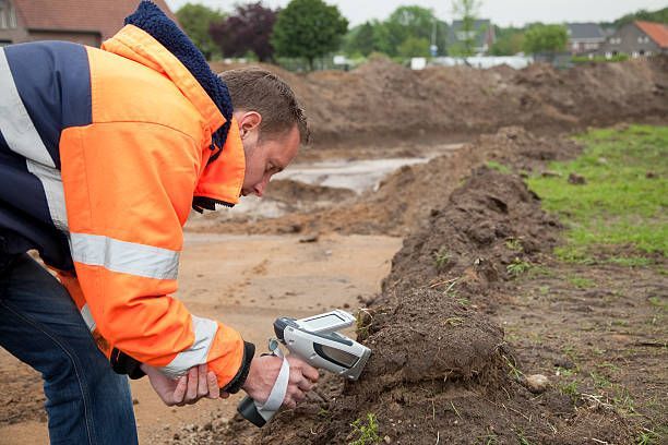 A man in an orange jacket is using a metal detector to examine a pile of dirt.