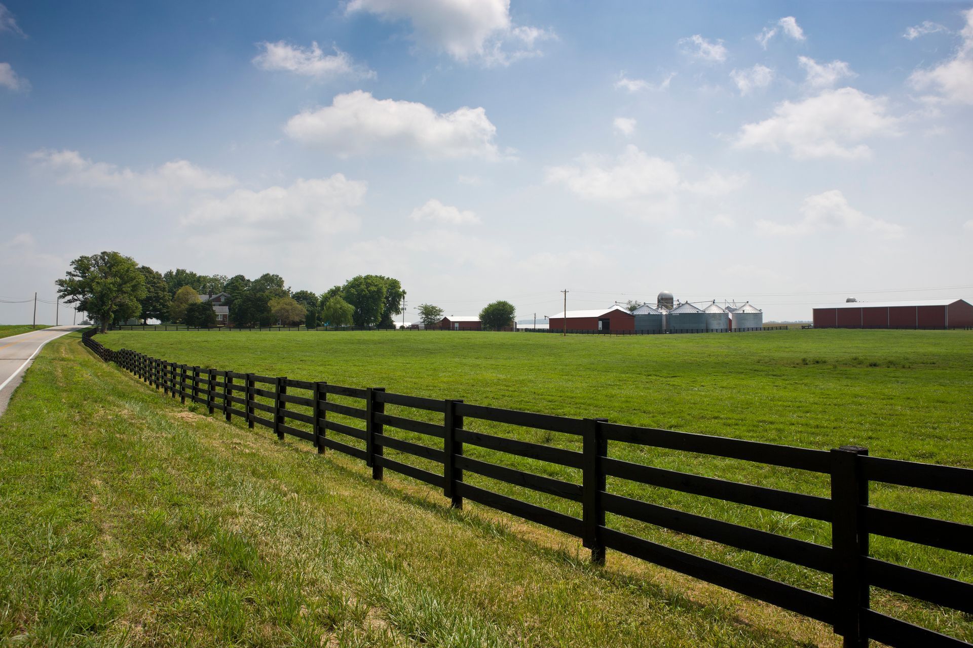 A black fence surrounds a grassy field with a barn in the background.