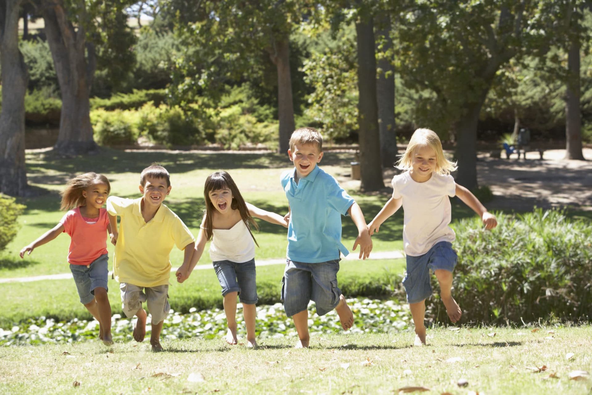 Children running hand in hand through a sunny park, smiling among trees and grass