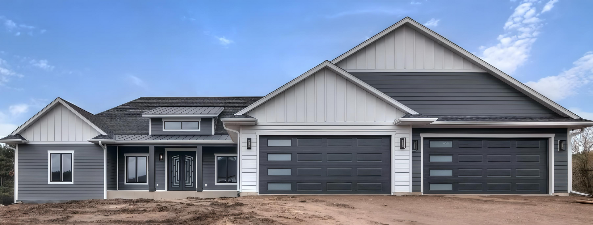 A large house with a lot of windows and garage doors is sitting on top of a dirt hill.