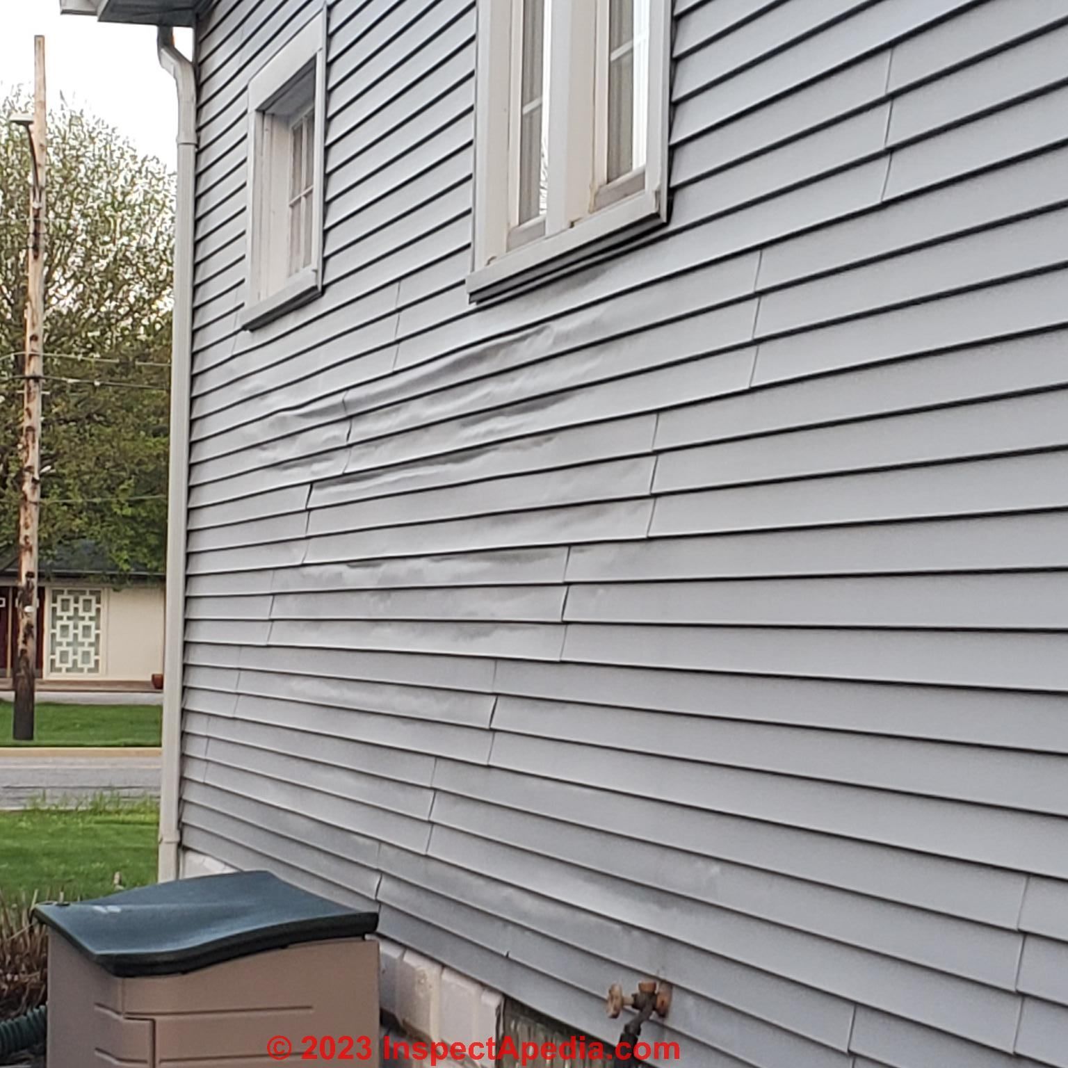 The side of a house with a gray siding and two windows.