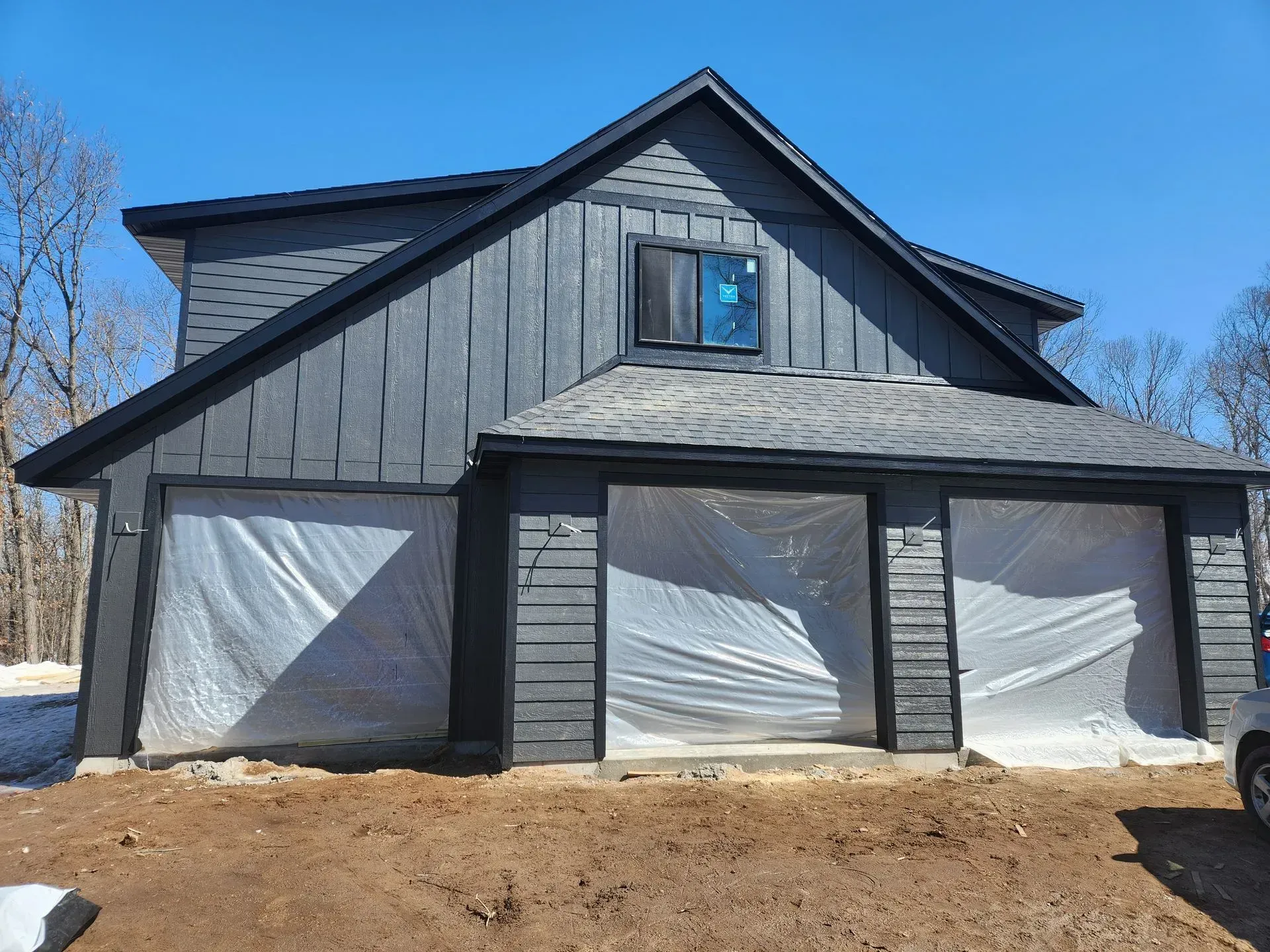 A gray house with a black roof is covered in plastic.