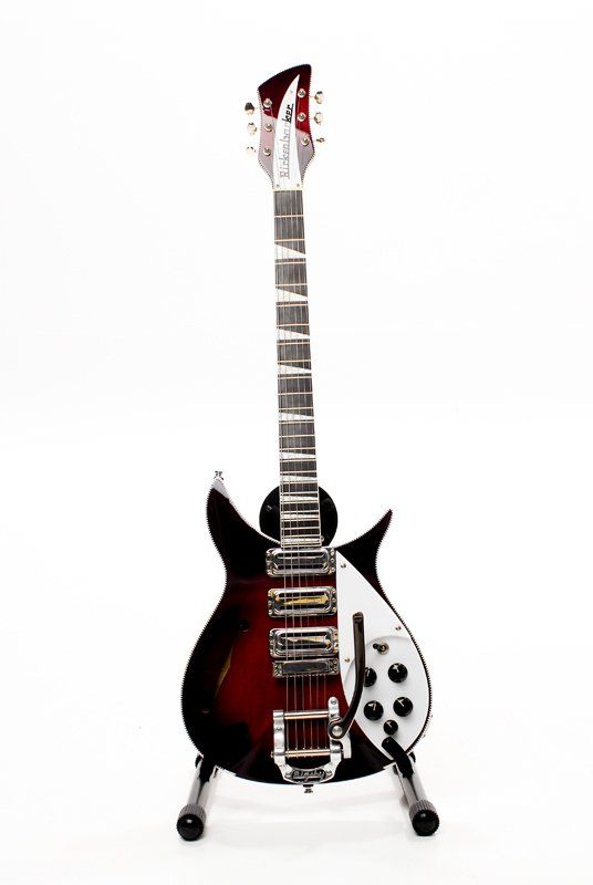 A red and black electric guitar is sitting on a stand on a white background.