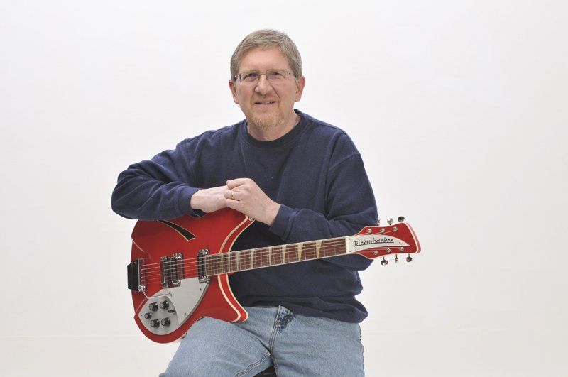 A man is sitting on a stool holding a red guitar