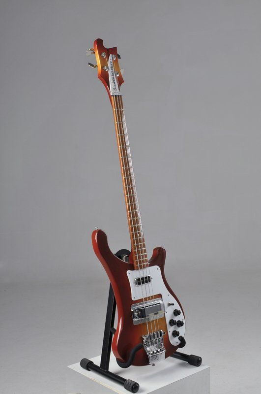 A red electric guitar is sitting on a stand on a white cube.