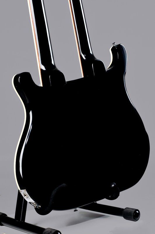 A black double neck guitar is sitting on a stand