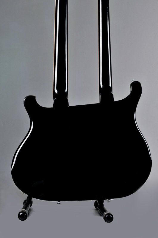 A black double neck electric guitar is sitting on a stand.