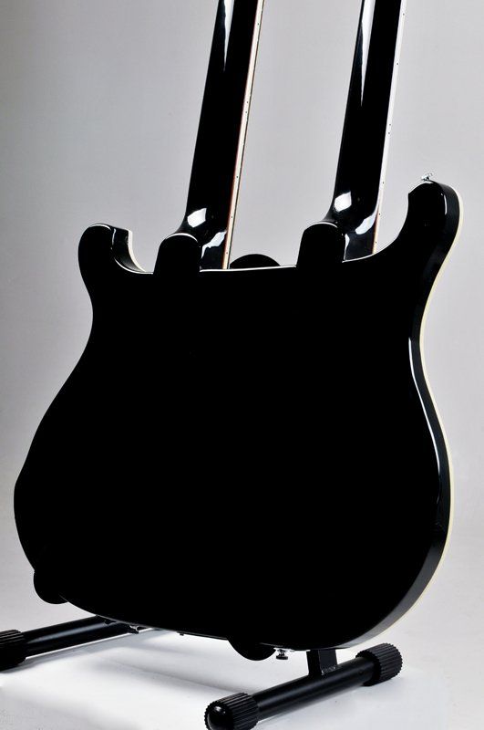 A black double neck guitar is sitting on a stand.