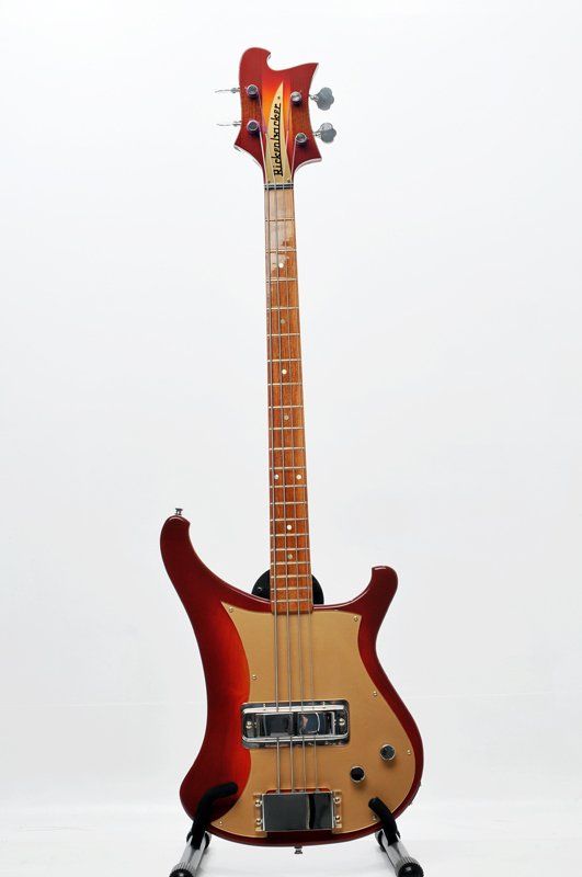 A red rickenbacker bass guitar is sitting on a stand