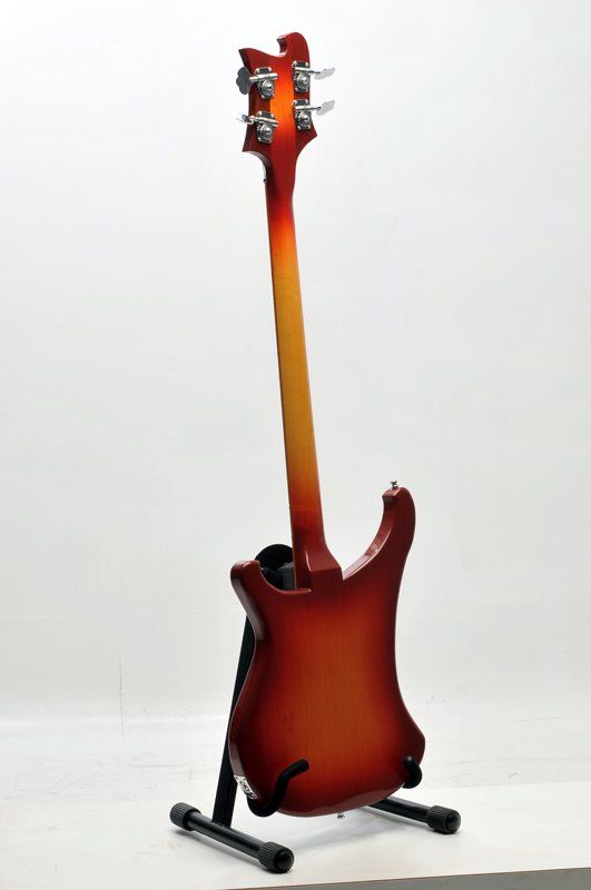 A red electric guitar is sitting on a stand on a white surface.