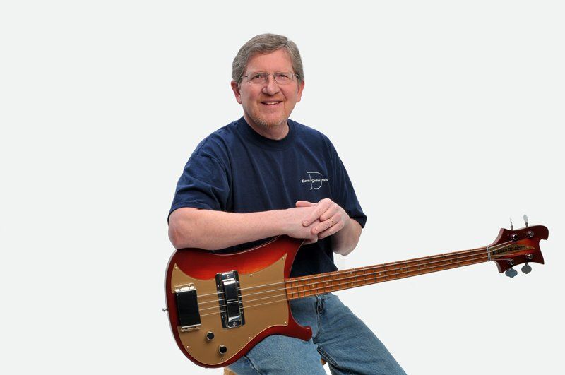 A man is sitting on a stool holding a red bass guitar.