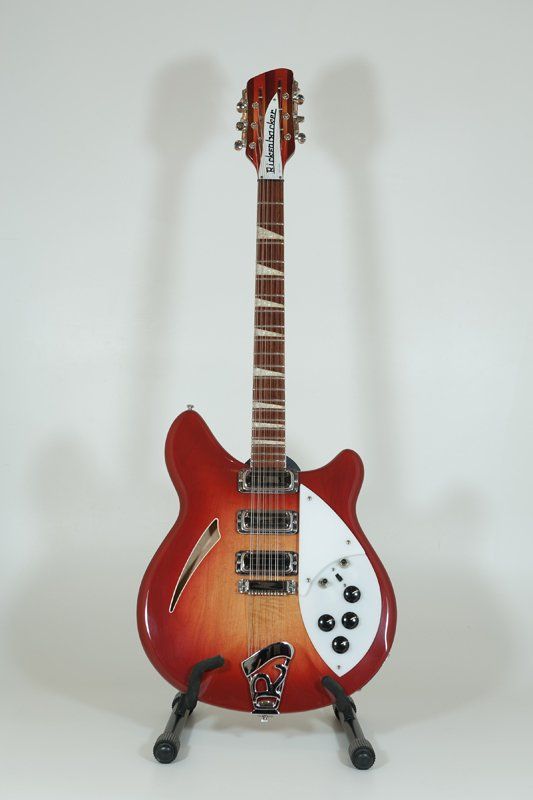 A red electric guitar is sitting on a stand on a white surface.