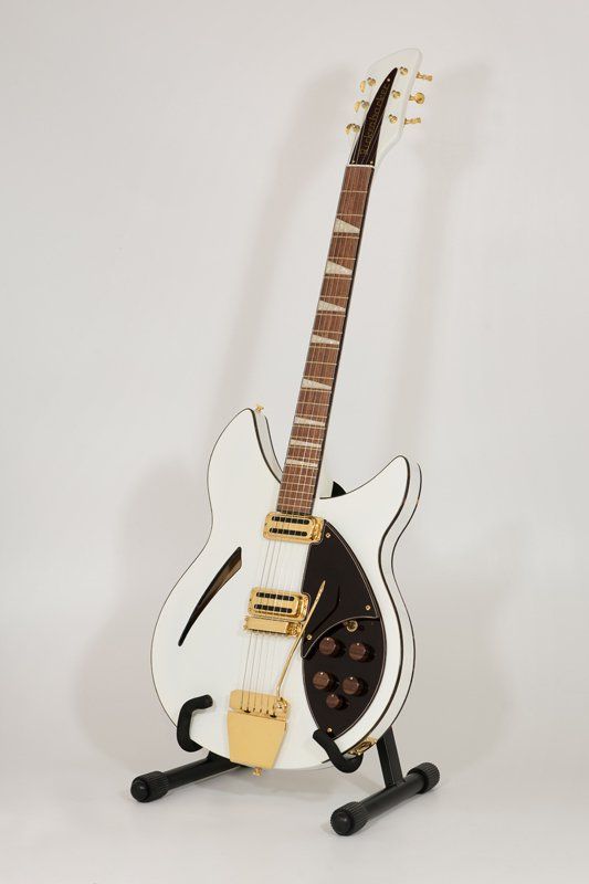 A white electric guitar is sitting on a stand.