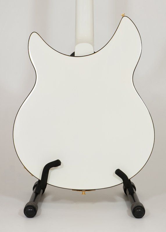 A white guitar is sitting on a stand on a white surface.