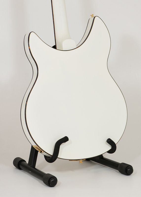 A white guitar is sitting on a black stand