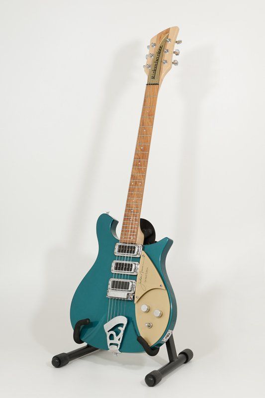 A blue electric guitar is sitting on a stand on a white background.