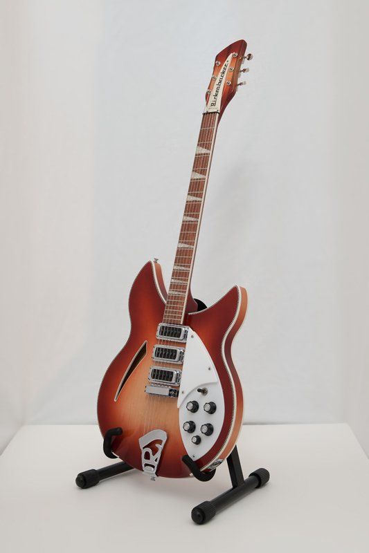 A red guitar is sitting on a stand on a table.