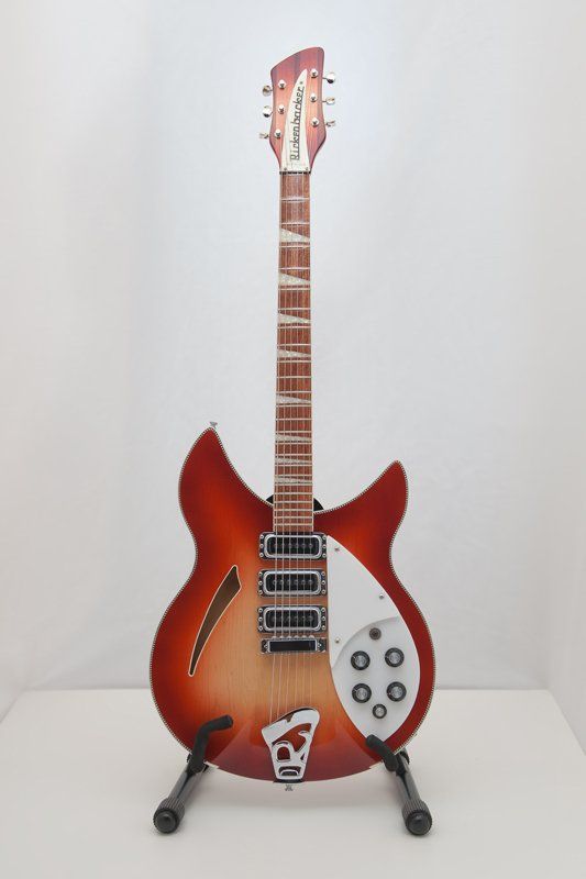 A red electric guitar is sitting on a stand on a white table.
