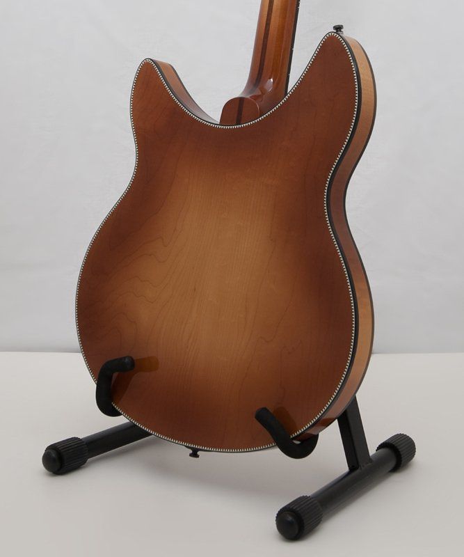 A brown guitar is sitting on a black stand