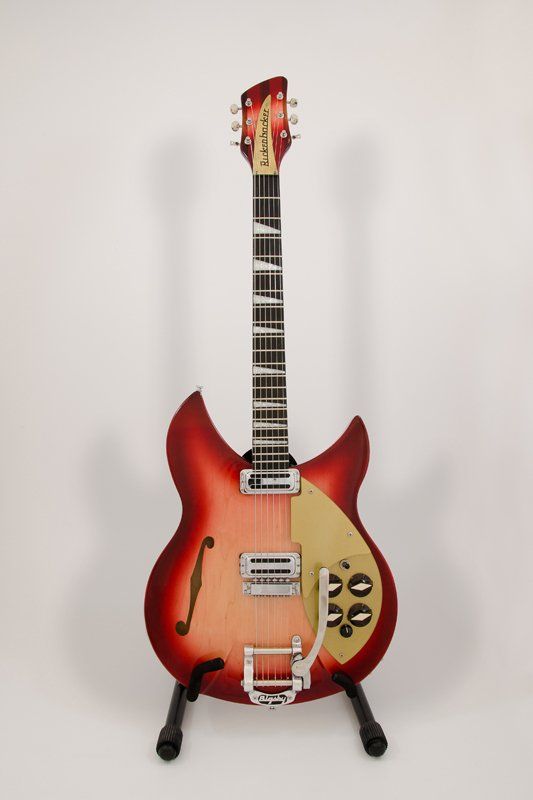 A red guitar is sitting on a stand on a white background