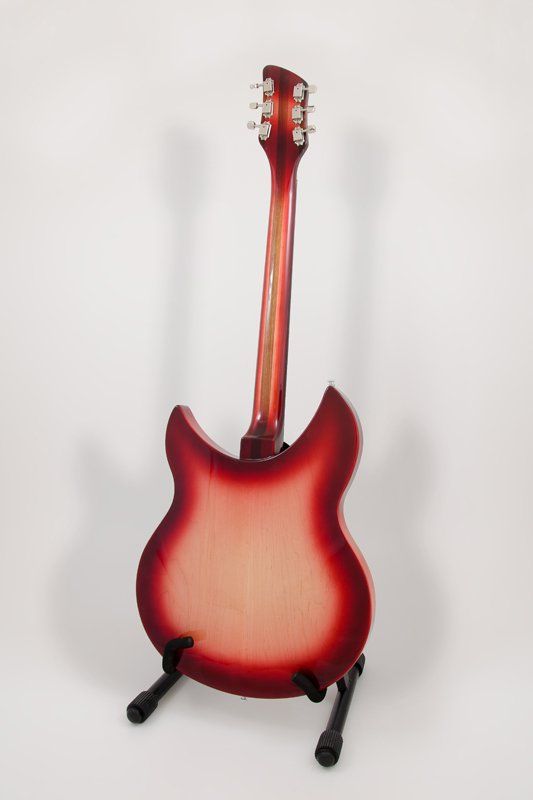 A red guitar is sitting on a stand on a white surface.