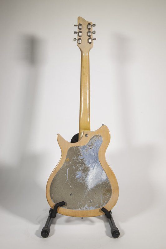 A guitar is sitting on a stand on a white surface.