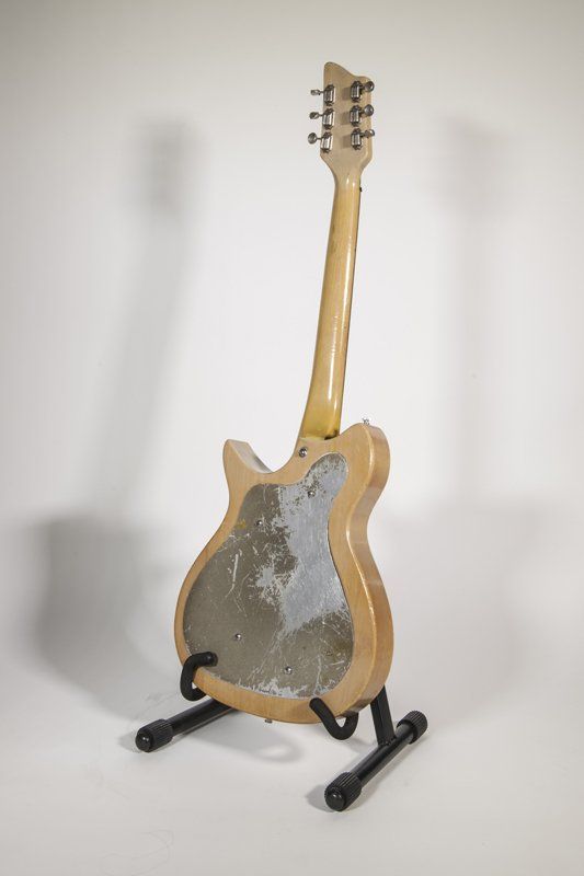 A guitar is sitting on a stand on a white surface.