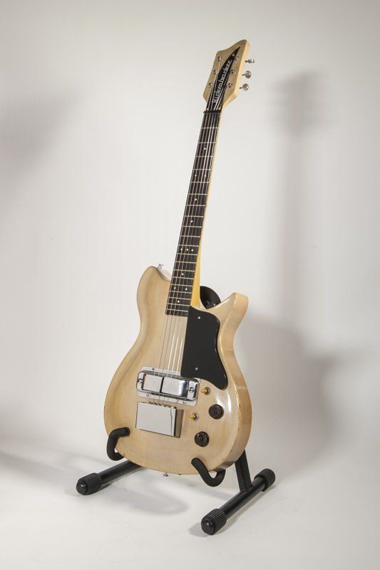 A guitar is sitting on a stand on a white surface.