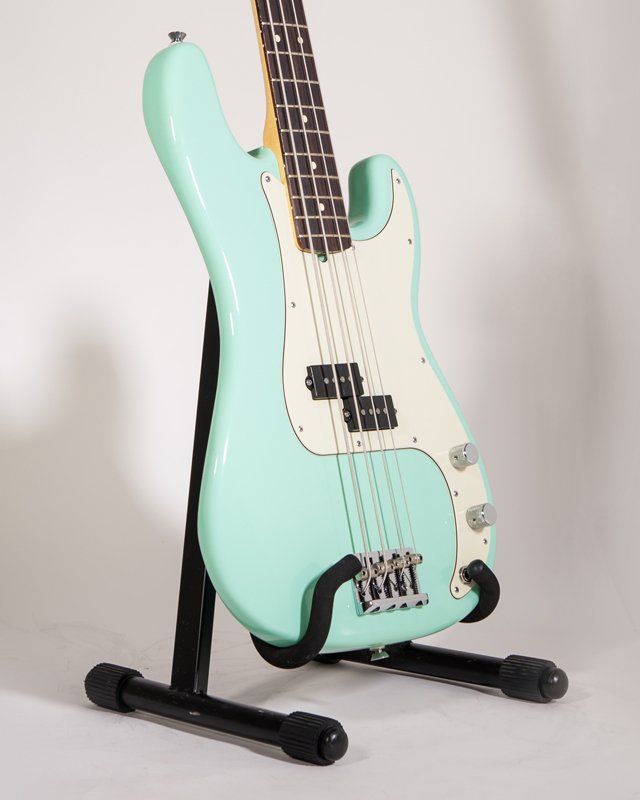 A mint green bass guitar is sitting on a black stand
