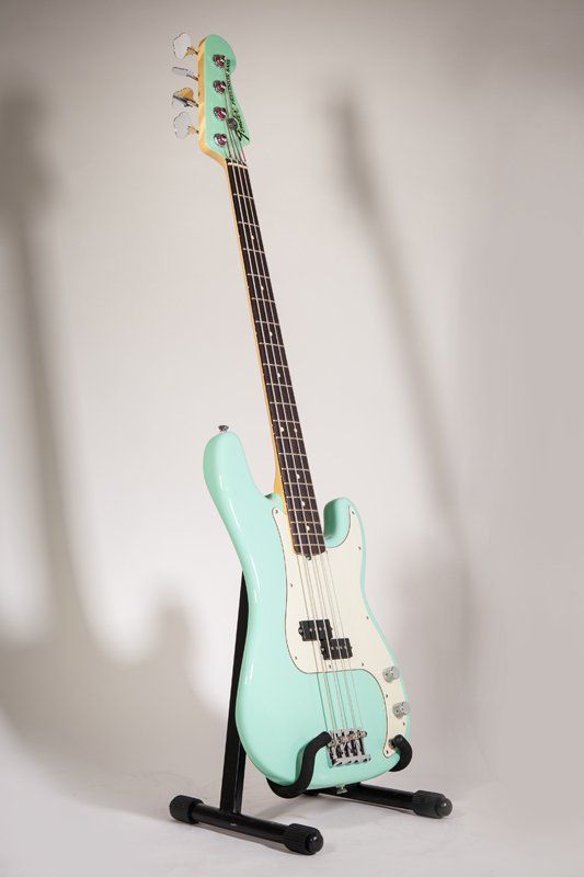 A mint green electric bass guitar is sitting on a stand.