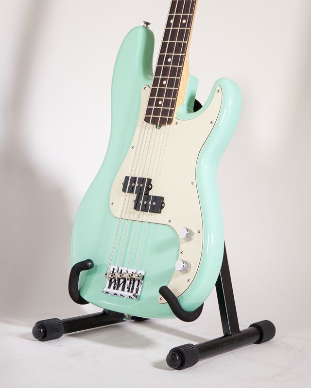 A mint green bass guitar is sitting on a black stand