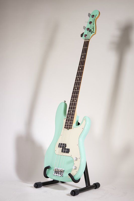 A mint green electric bass guitar is sitting on a stand.