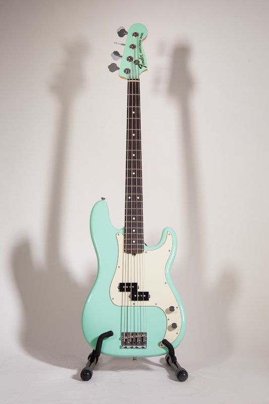 A mint green electric bass guitar is sitting on a stand.