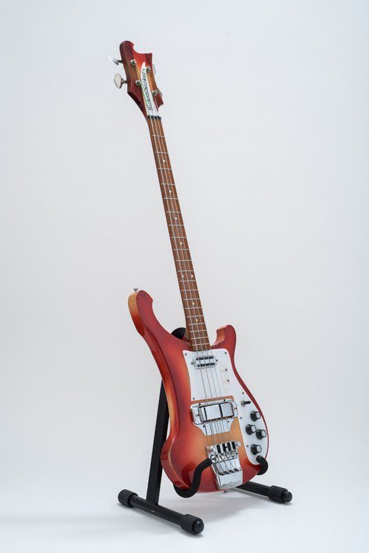 A red electric guitar is sitting on a stand on a white background.