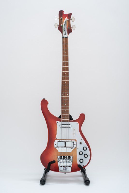 A red rickenbacker bass guitar is sitting on a stand