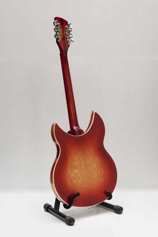 A red electric guitar is sitting on a stand on a white surface.
