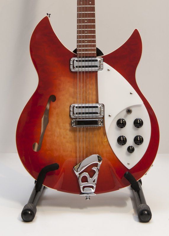 A red rickenbacker guitar is sitting on a stand
