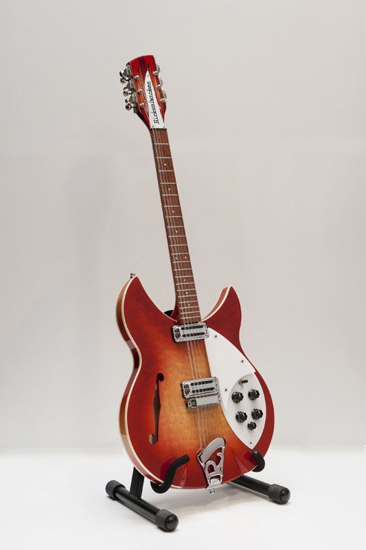 A red guitar is sitting on a stand on a white surface.