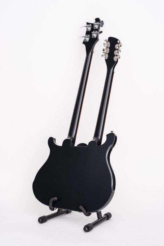 A black double neck guitar is sitting on a stand.